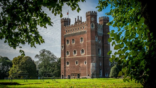 Tattershall Castle's Great Tower surrounded by blue sky and bright green leaves on branches are seen near the edges of the picture